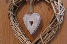 Holzherz hängt an einem geflochtenen Kranz aus Naturmaterialien. Gemütliche Dekoration für Unterkunft.