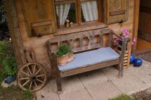 Holzbank vor einem rustikalen Haus, umgeben von Pflanzen und dekorativen Elementen.